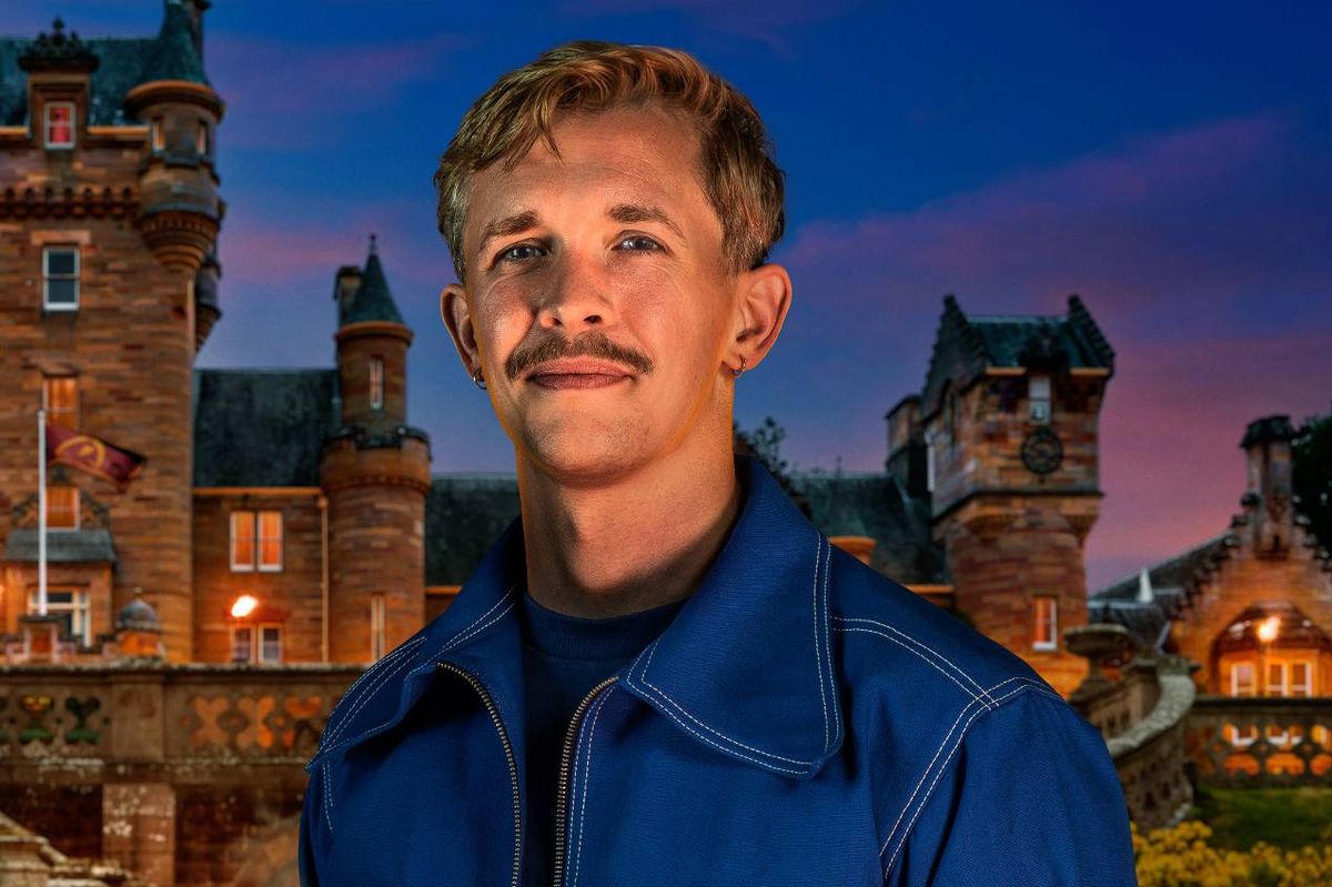 An individual dressed in a blue jacket stands in front of a historic building, with a backdrop of a twilight sky.