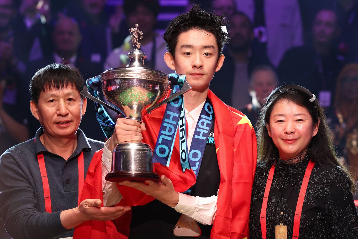 China's Wu Yize (C) holds the championship trophy as he poses with his parents during the awards ceremony after his victory over England's Shaun Murphy in the World Snooker Championship final round at The Crucible in Sheffield, northern England on May 4, 2026. 