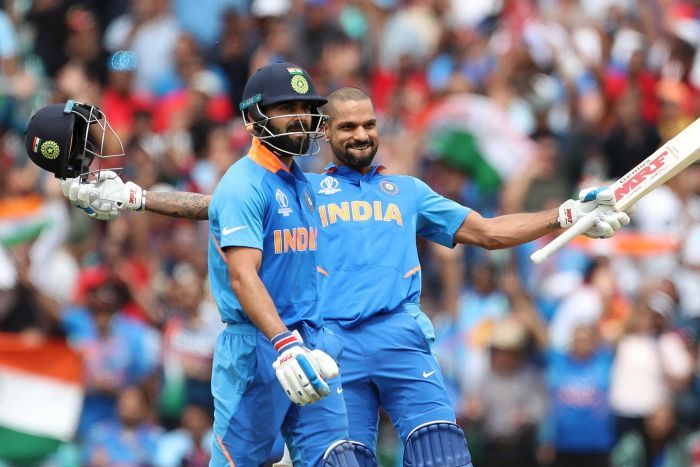 Shikhar Dhawan celebrates a century Shikhar Dhawan leans back with arms outstretched. He is smiling and has his helmet removed. Virat Kohli stands in the foreground