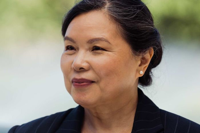 Wai Ling A headshot of a woman in a suit in front of some trees.