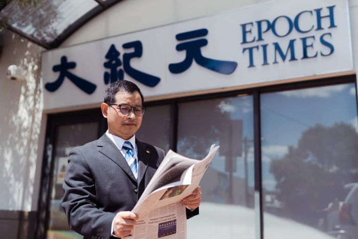 Epoch Times A man in a suit reads a newspaper outside the Epoch Times office.