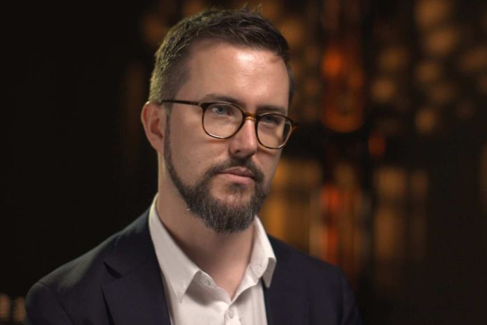 Fergus Ryan Head shot of Fergus Ryan wearing open-collared white shirt, grey suit and glasses