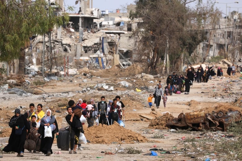 People carrying their belongings as they walk down a road in a town destroyed by artillery.