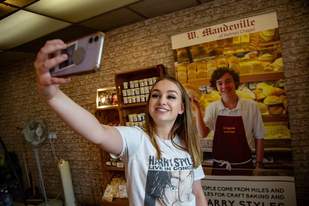 Posing for a selfie with a picture of a young Harry Styles at the bakery he used to work at