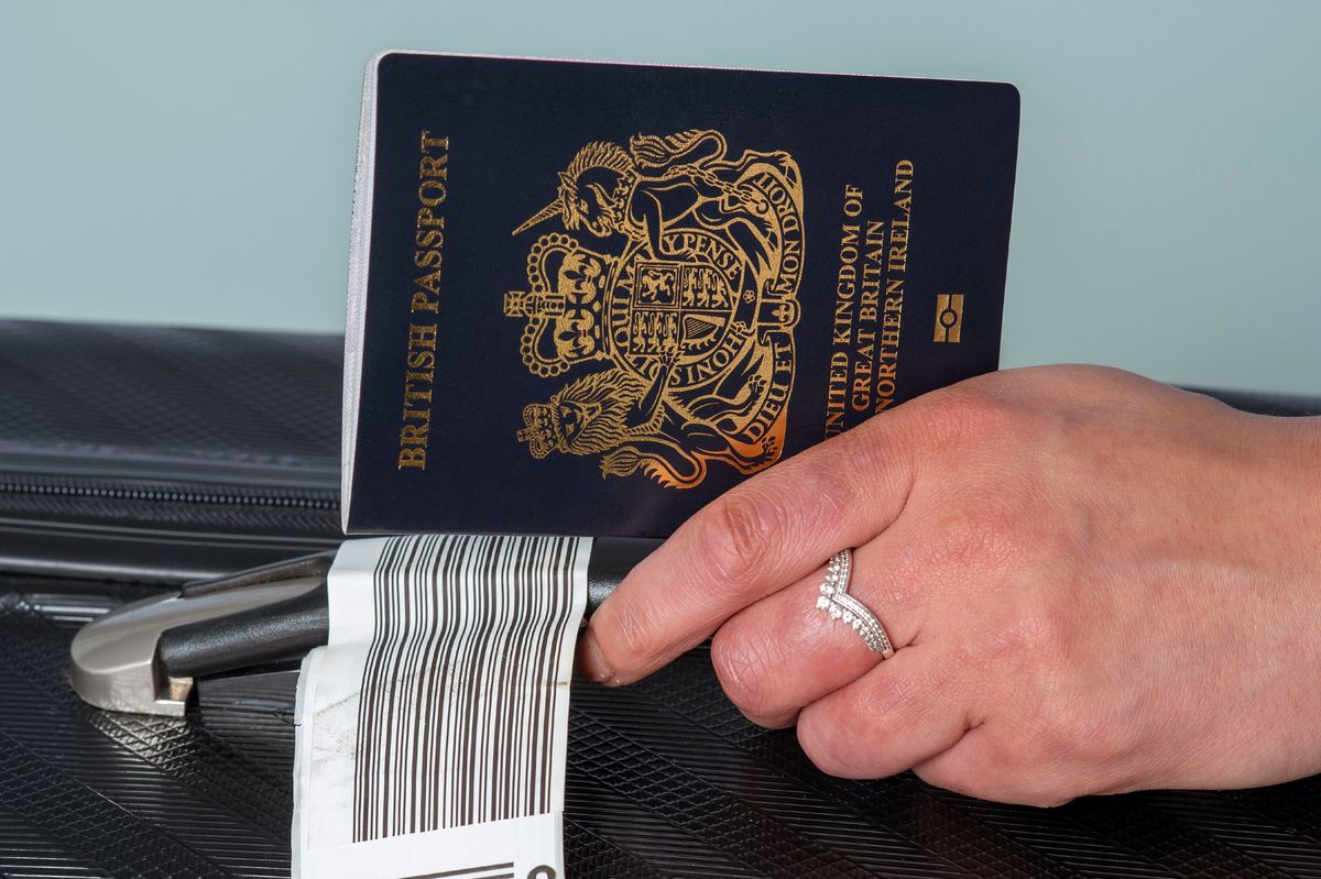 In this photo illustration, a new dark blue colored British passport held in a travellers hand with holiday suitcase.