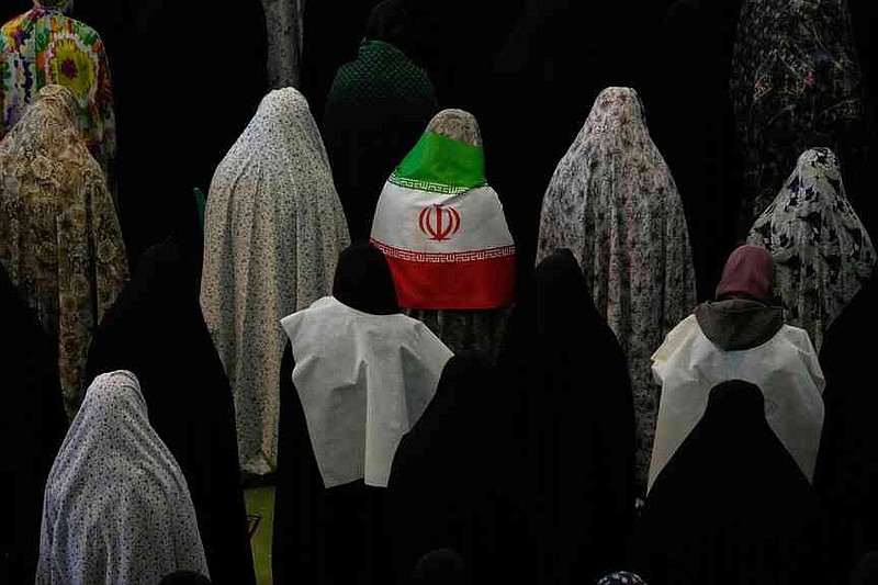 Iranian worshippers perform Eid al-Fitr prayers marking the end of the holy fasting month of Ramadan as one of them wears an Iranian flag at the Imam Khomeini Grand Mosque in Tehran, Iran, Saturday, March 21, 2026. (AP Photo/Vahid Salemi)