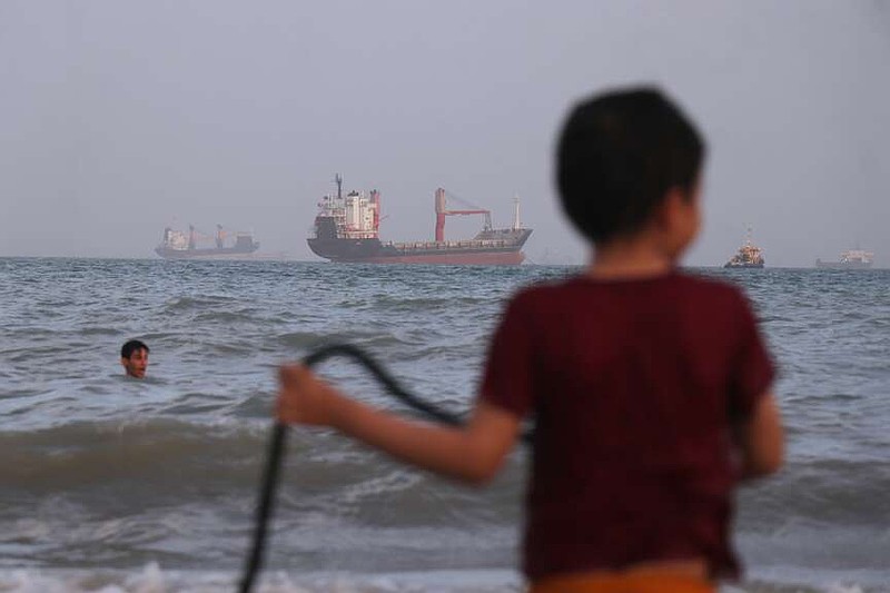 Children play in the water along the shore as a mix of bulk carriers, cargo ships, and service vessels sit offshore in the Strait of Hormuz off Bandar Abbas, Iran, Sunday, April 26, 2026.(Razieh Poudat/ISNA via AP)