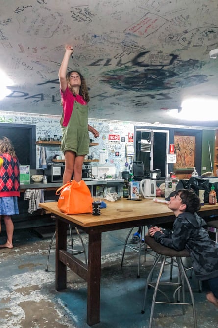 A girl standing on a table in a backpackers' hostel, holding up a pen to add to all the writing on the ceiling