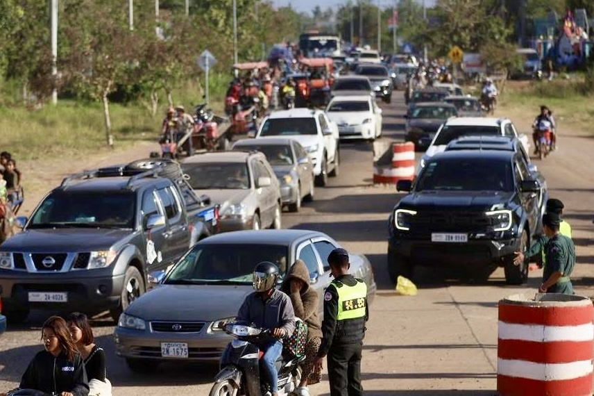 People evacuating in cars and on motorbikes along a street, with a police officer directing traffic.
