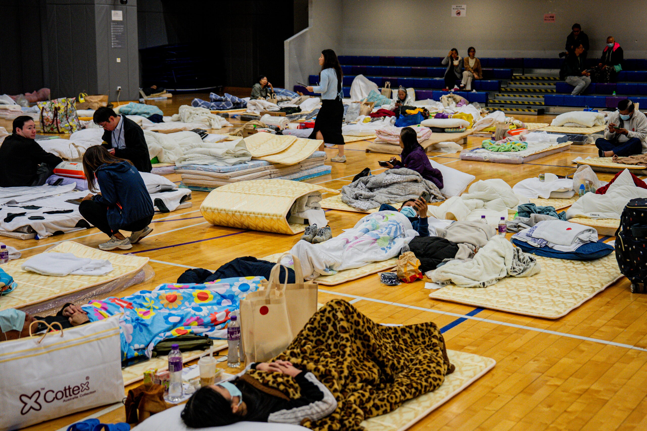 People rest on mats on a wooden floor at an emergency shelter.