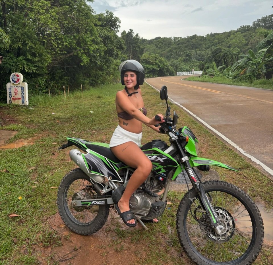 A young woman sitting on a green motorcycle on a road in Thailand.