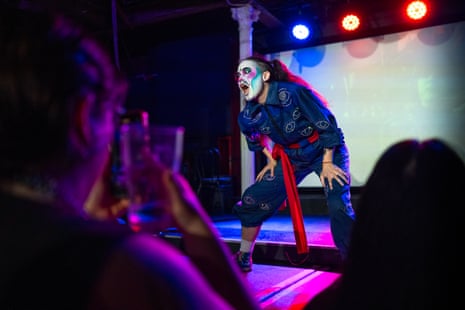 A heavily made-up performer with long hair and wearing a blue jumpsuit adorned with silver eyes entrances the crowd