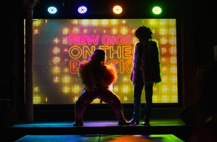 Two figures in silhouette with a brightly lit sign saying ‘New gigs on the block’ behind them