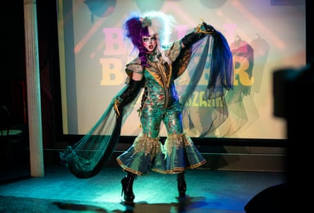 Figure in a shiny blue outfit with bell trouser legs and chiffon shawl
