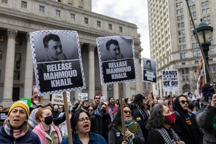 crowd of people hold signs in front of white building