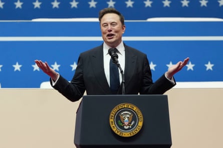 man wearing black suit and tie holds arms up while speaking behind podium