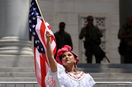A woman, wearing a traditional Mexican dress, holds an American flag