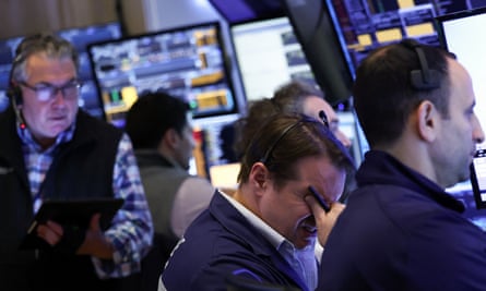 Stock market traders look at walls of screens while one person holds their head in their hand