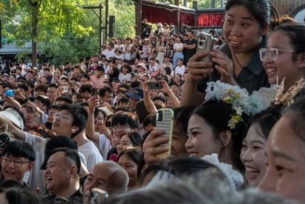 A crowd of people, many of them young women, hold up phones and laugh.