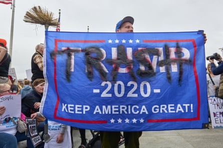 A person waves a Trump 2020 flag that has been overwritten in black spray paint with the word “trash”
