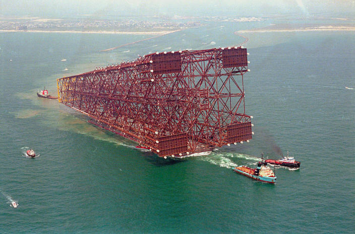 An oil platform on its side with tugboats surrounding it in the water