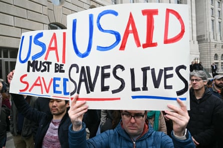 people holding signs that say ‘USAid saves lives’ and ‘USAid must be saved’