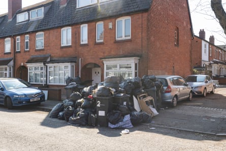 Piles of black sacks of rubbish in the road on a corner by redbrick houses.