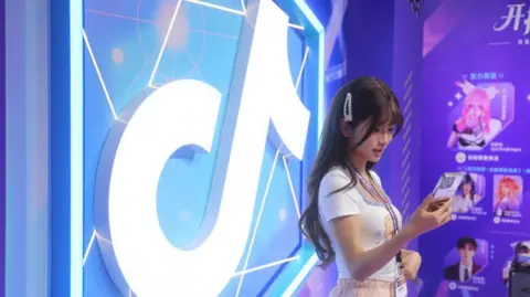 Getty Images Woman standing in front of a brightly-lit and colourful TikTok logo while looking at her smartphone