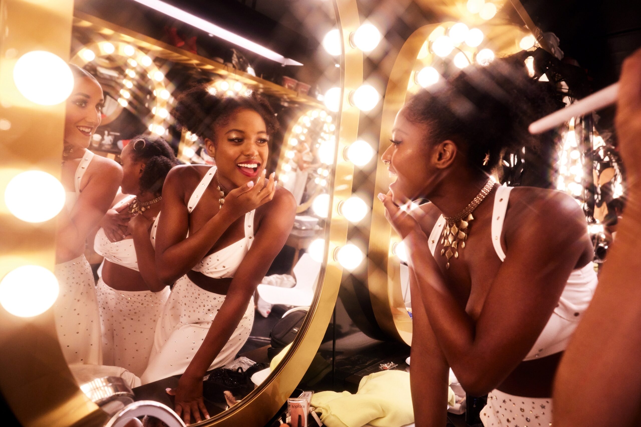 An immersive shot of girls dressed up to go out, touching up their make-up in an illuminated mirror.