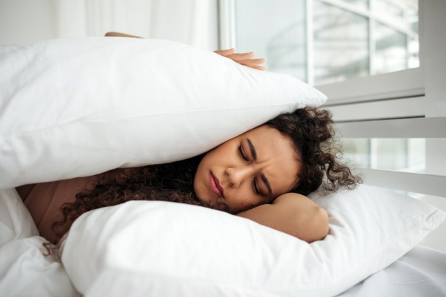 A dark-skinned woman lies on the bed and covered herself with pillows. Heavy morning. Awakening. Loud noise during sleep.