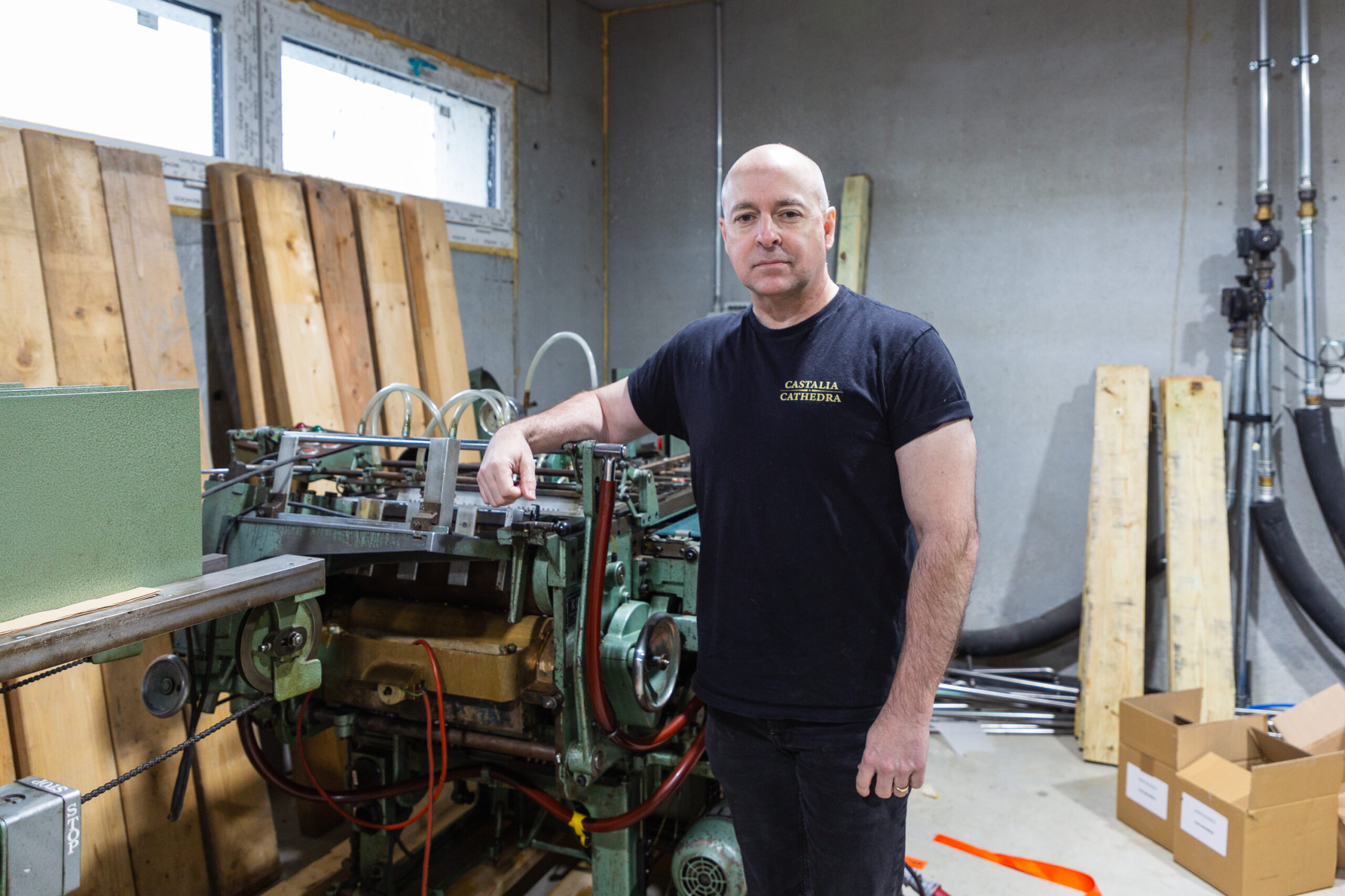 Vox Day stands next to a machine, wooden boards in the background