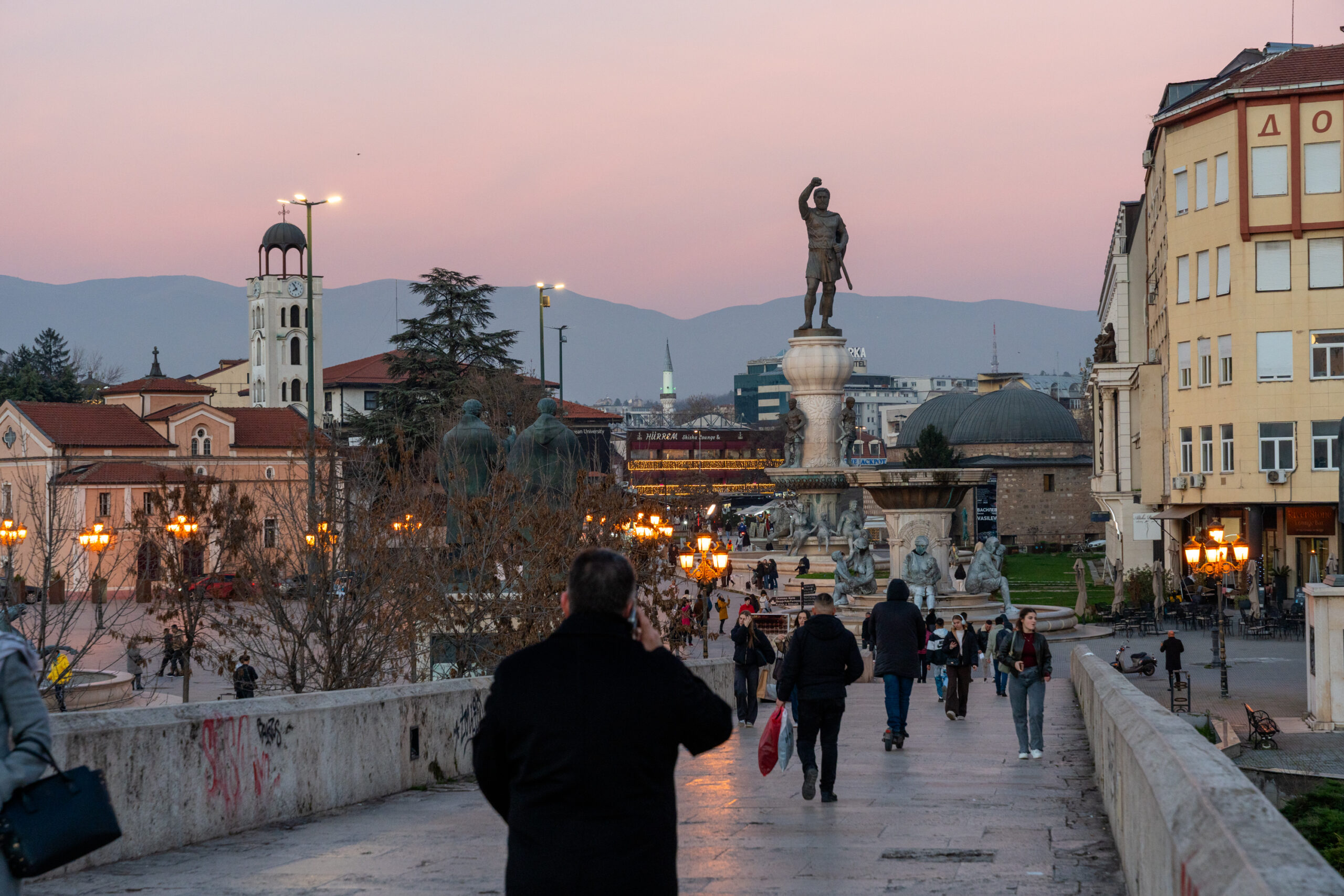A busy square at dusk with a large statue and people on the pavement