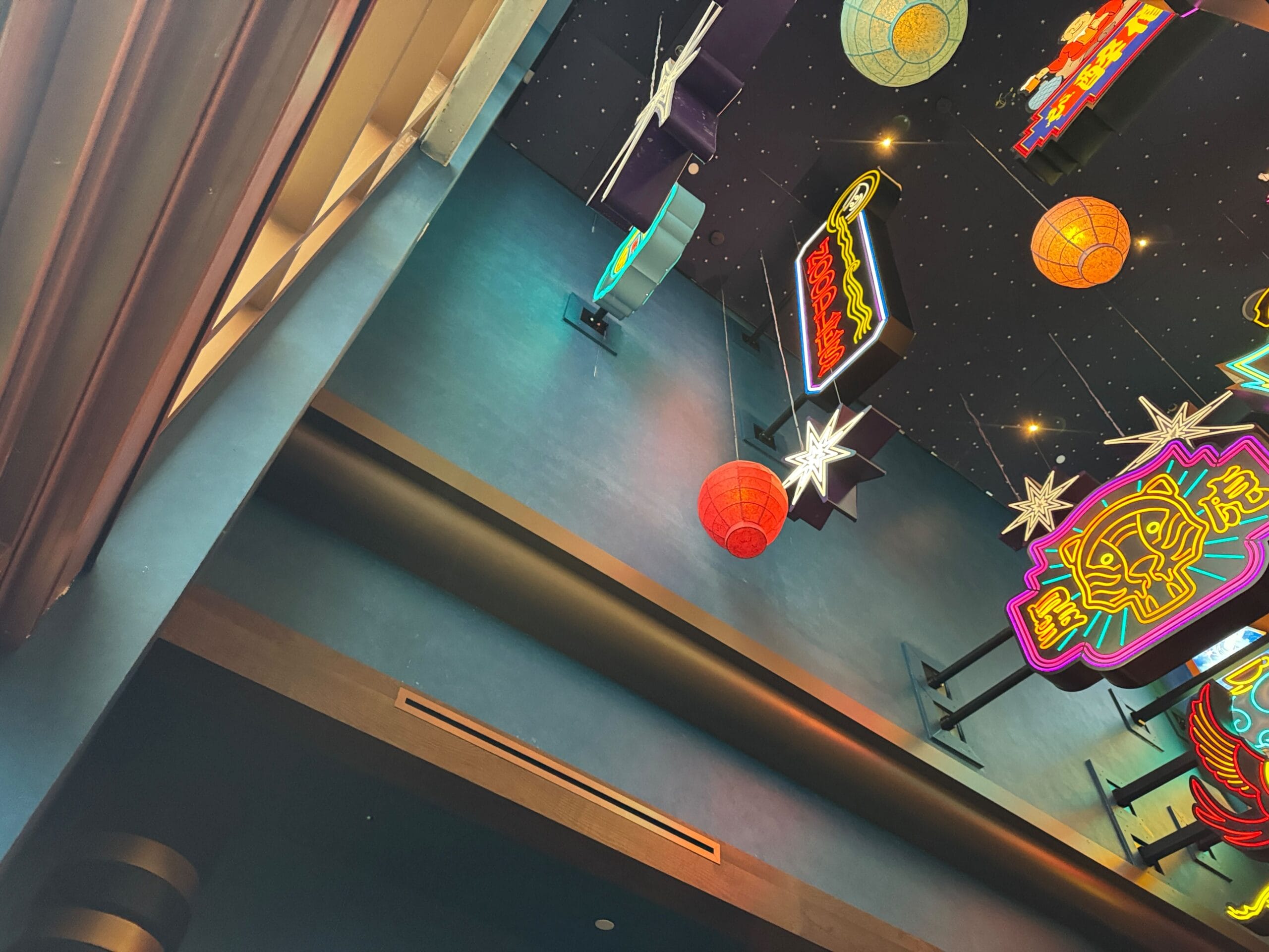 Colorful neon signs and lanterns hang from a starry ceiling above a blue wall and window curtains.