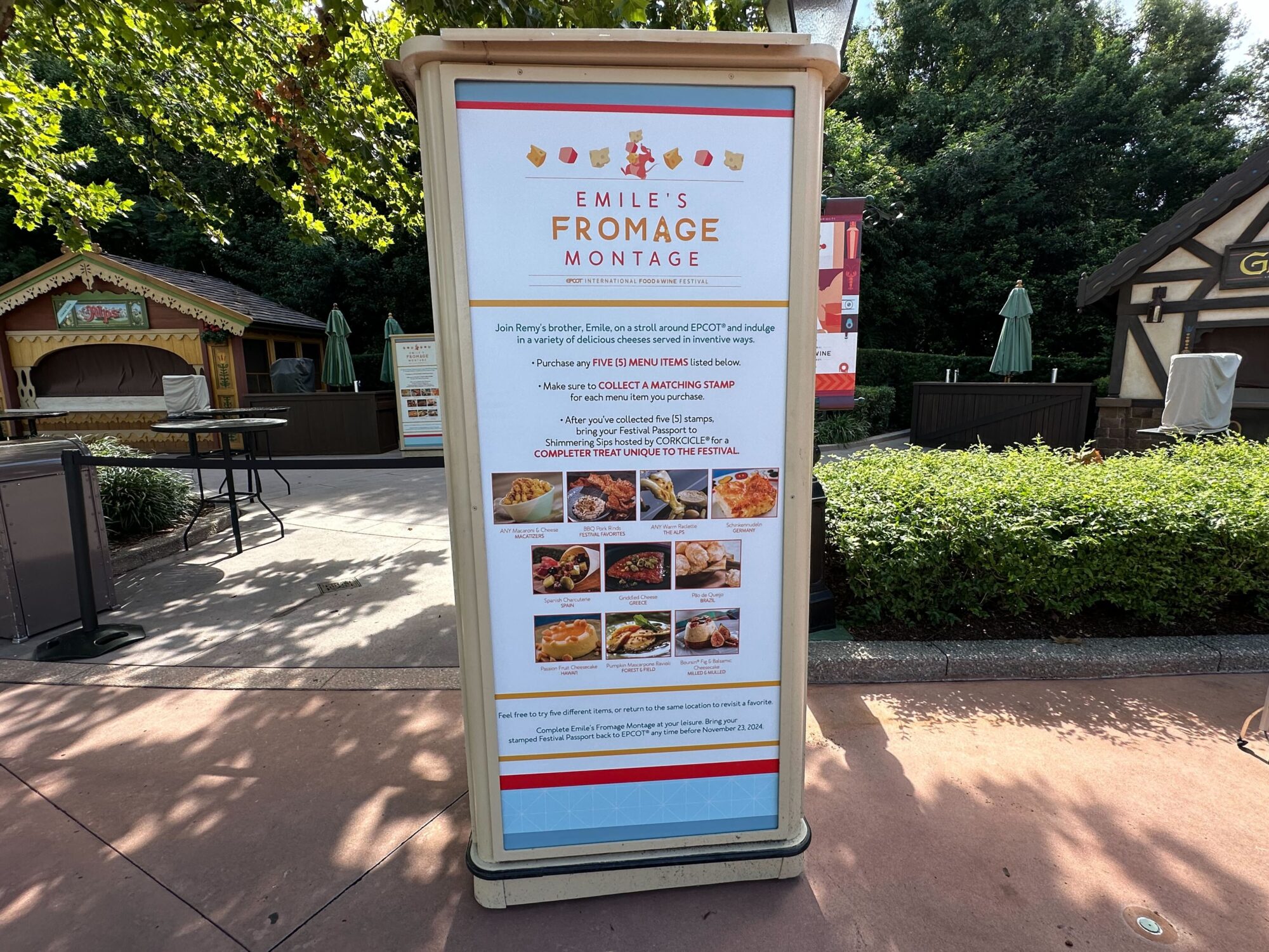 Menus (With Prices) for 2024 EPCOT International Food & Wine Festival 76 A signboard for Emile's Fromage Montage stands outdoors, displaying promotional text and images of various cheese dishes, with details on how to participate in a culinary challenge at EPCOT.