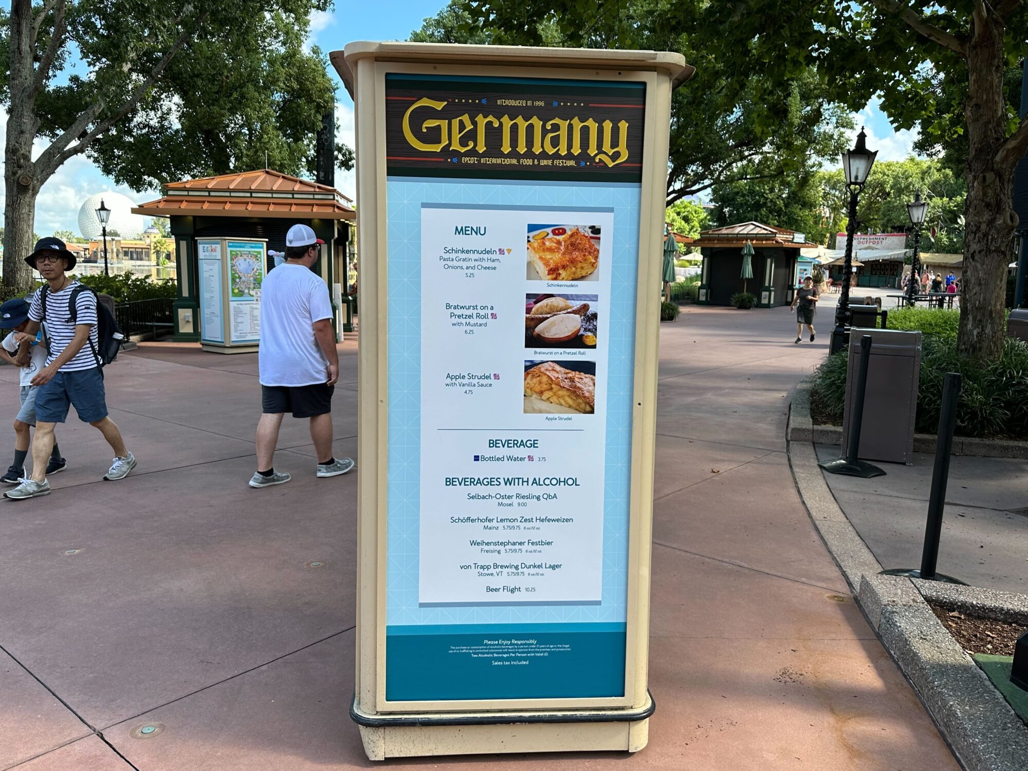 Menus (With Prices) for 2024 EPCOT International Food & Wine Festival 31 A signboard at the entrance of the Germany pavilion displaying a menu of food and beverages, including items like Schinkennudeln, Apple Strudel, and a variety of alcoholic drinks.