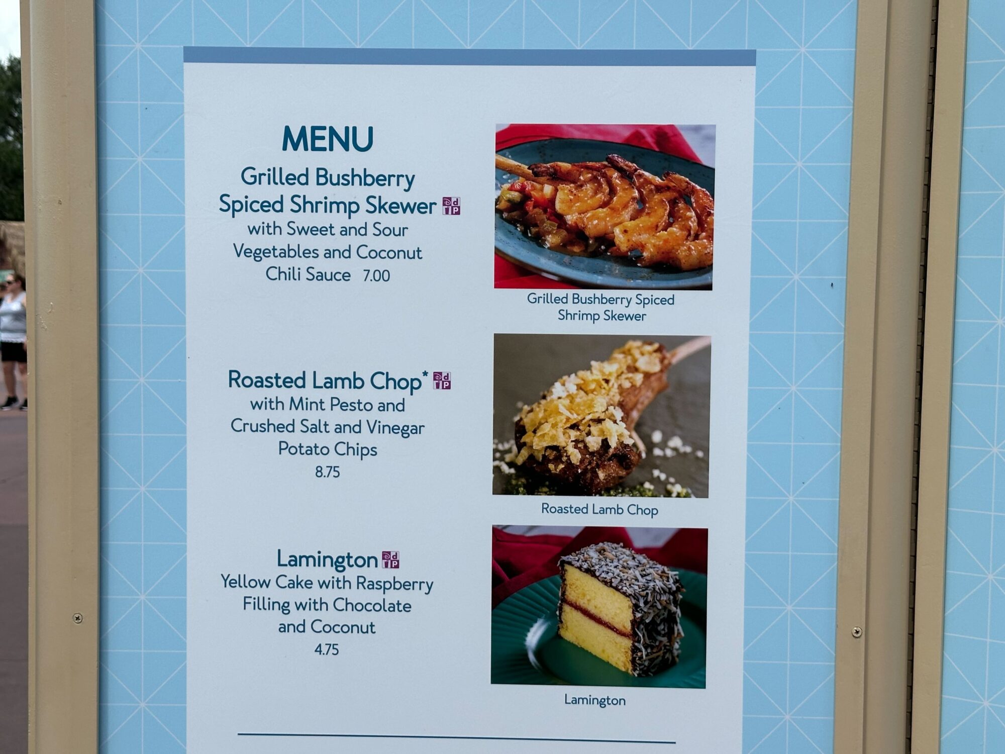 Menus (With Prices) for 2024 EPCOT International Food & Wine Festival 14 Image of a festival menu featuring three dishes: Grilled Bushberry Spiced Shrimp Skewer, Roasted Lamb Chop with mint pesto and salt and vinegar potato chips, and Lamington with raspberry filling, chocolate, and coconut.