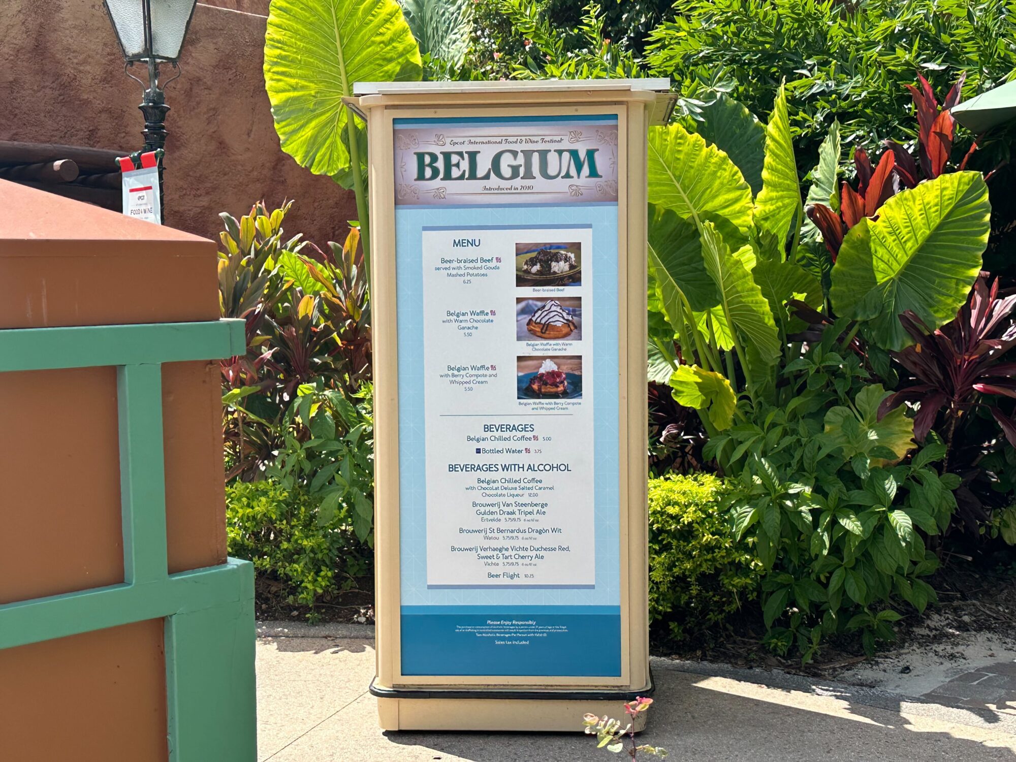 Menus (With Prices) for 2024 EPCOT International Food & Wine Festival 47 A menu board at the food & wine festival showcases delicious options from Belgium, including Belgian waffles and beer. Surrounded by lush green foliage, the outdoor setting adds a charming touch to the experience.