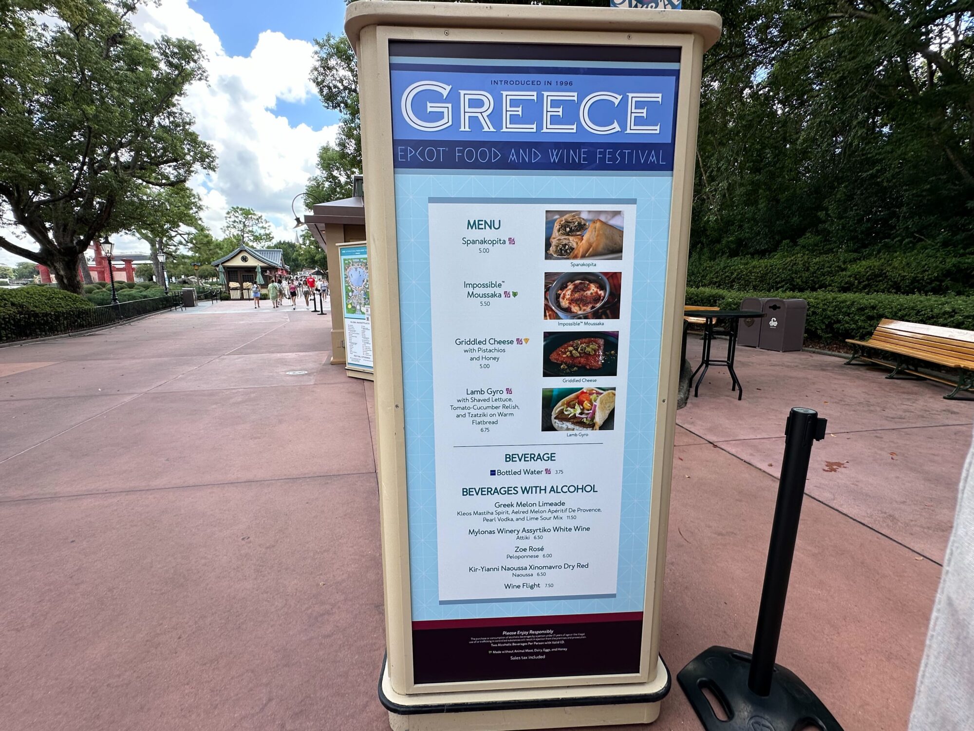 Menus (With Prices) for 2024 EPCOT International Food & Wine Festival 43 A sign for the Greece booth at the Epcot Food & Wine Festival displays menus featuring Spanakopita, Impossible Moussaka, Griddled Cheese, and Lamb Gyros.