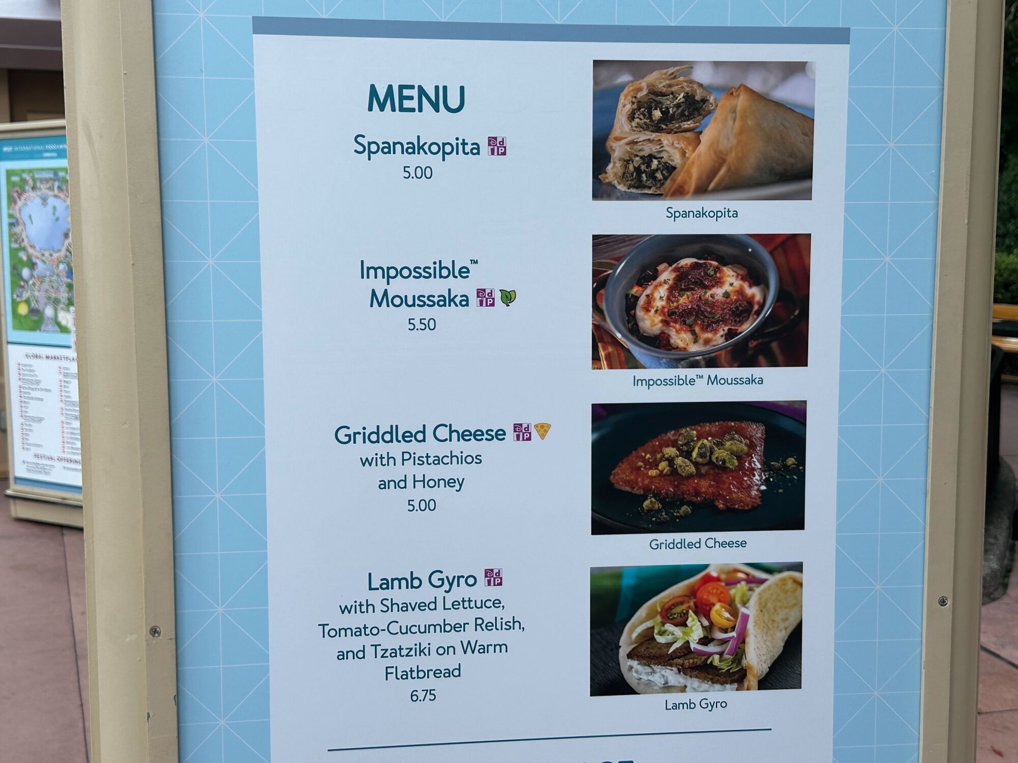 Menus (With Prices) for 2024 EPCOT International Food & Wine Festival 44 A menu at the food & wine festival showcases four items: Spanakopita for $5.00, Impossible Moussaka for $5.50, Griddled Cheese for $5.00, and Lamb Gyro for $6.75, complete with tempting descriptions and vibrant images of each dish.
