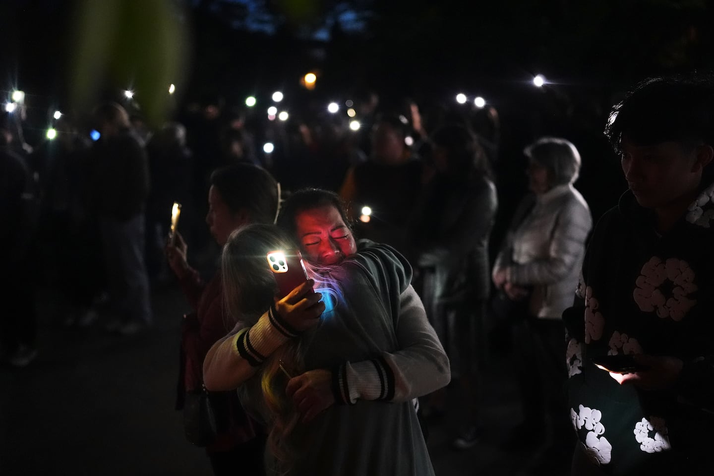 Liza Ahyeng, center right, hugs another attendee at a vigil for victims.