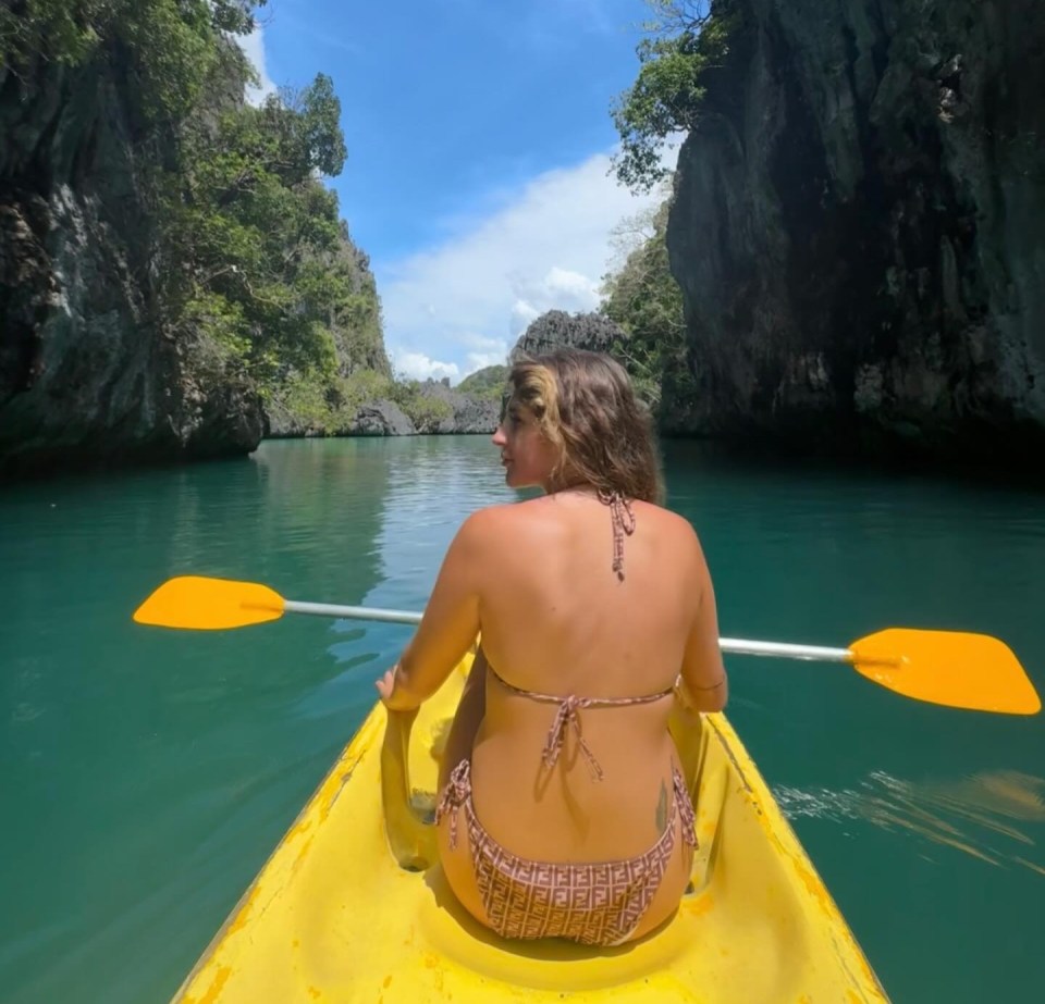 Woman kayaking through a narrow waterway between limestone cliffs.
