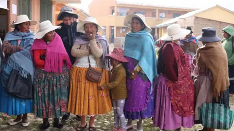 EPA/Shutterstock At least seven women in a line, smiling and laughing at the camera, wearing traditional, colourful Bolivian clothing, waiting to cast their vote in La Paz.