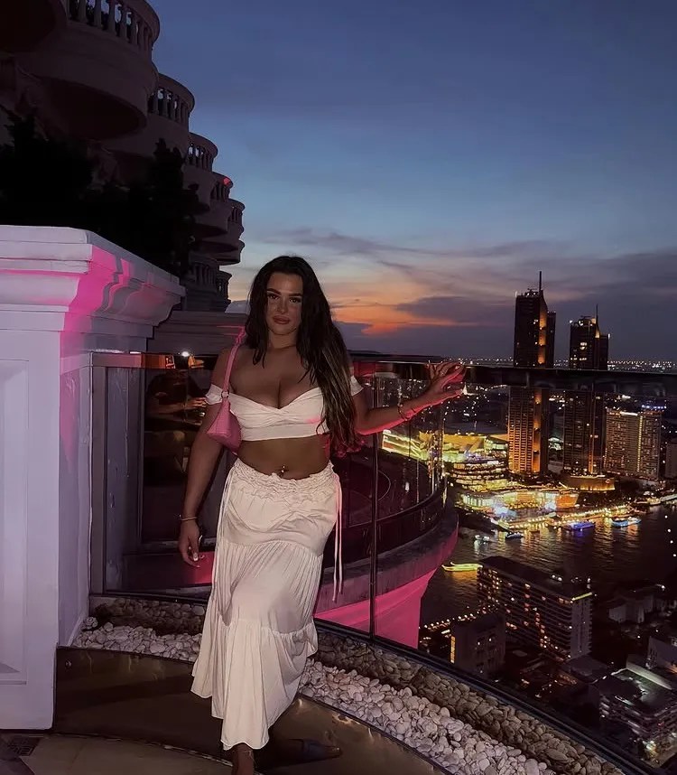 Woman in a white outfit on a rooftop overlooking a city at night.