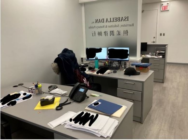 A photograph of the inside of Isabella Dan's law practice showing redacted legal documents on a desk and redacted computer screens.