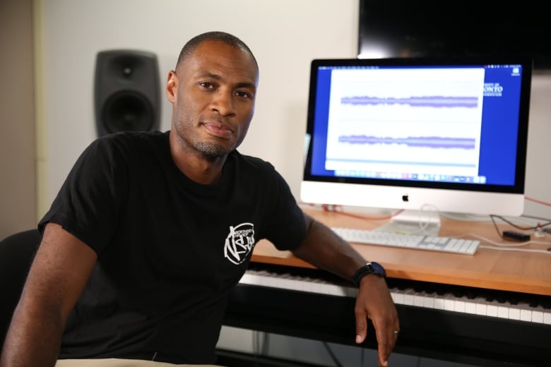 A man poses in front of a computer, with his arm against the desk.