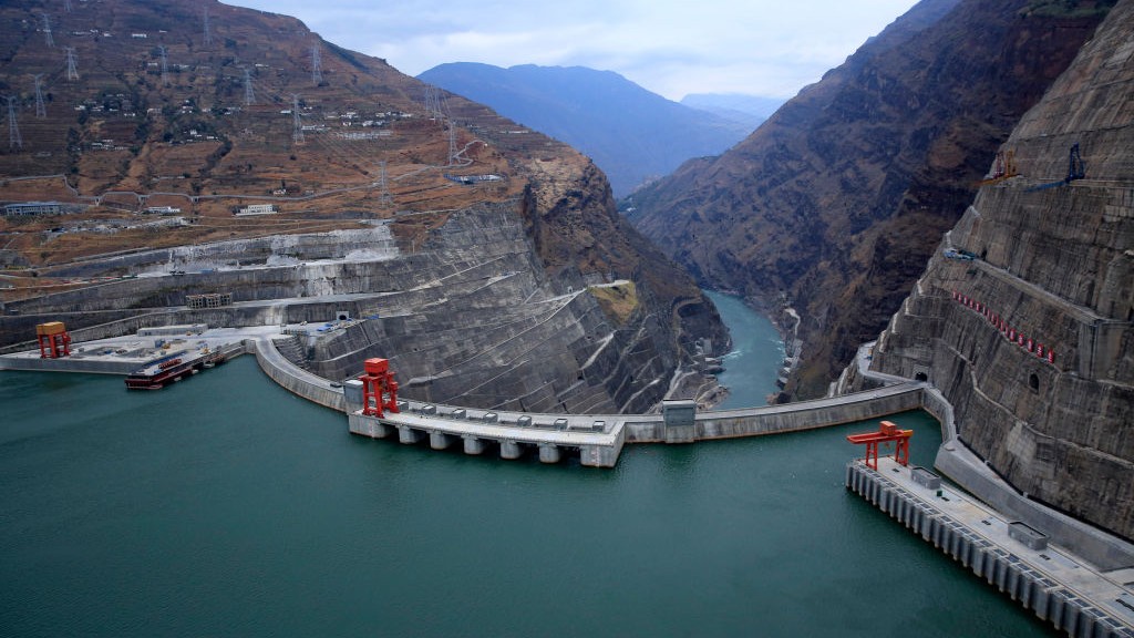 A huge hydroelectric dam in China. We see the reservoir in the foreground and a view of the valley beneath.