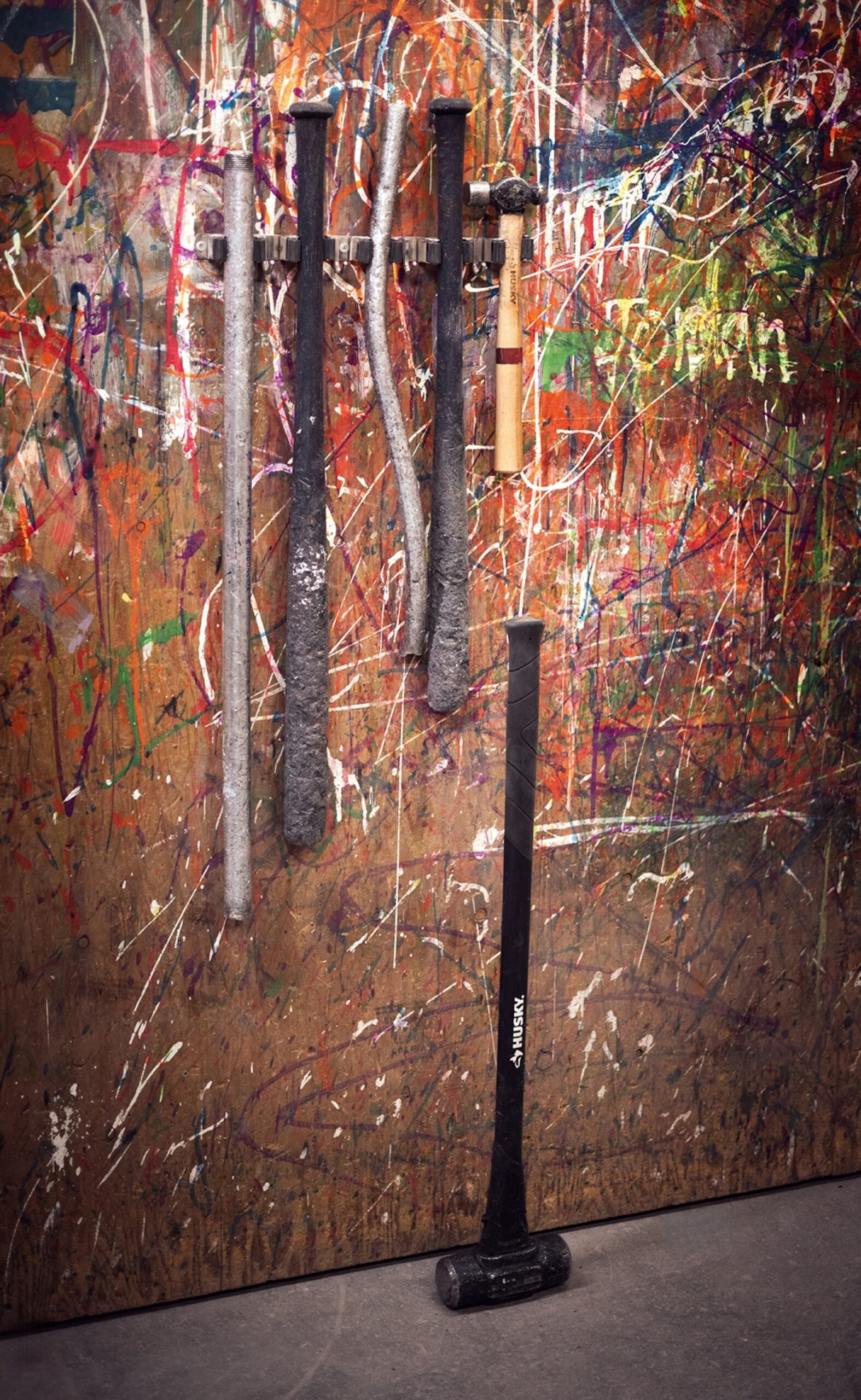 A close-up of bats and hammers hung on a plywood wall with trickles of paint.