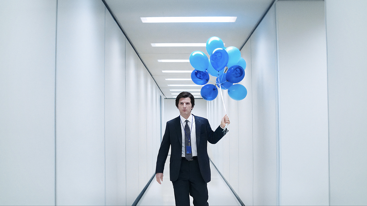 Mark walking down a bright, white hallway with blue balloons in Severance.