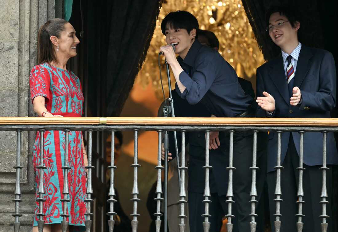 Jung Kook (center) and Suga (right) from South Korean K-pop band BTS acknowledge fans next to Mexico's President Claudia Sheinbaum from the balcony of the National Palace at Zocalo square in Mexico City on May 6.