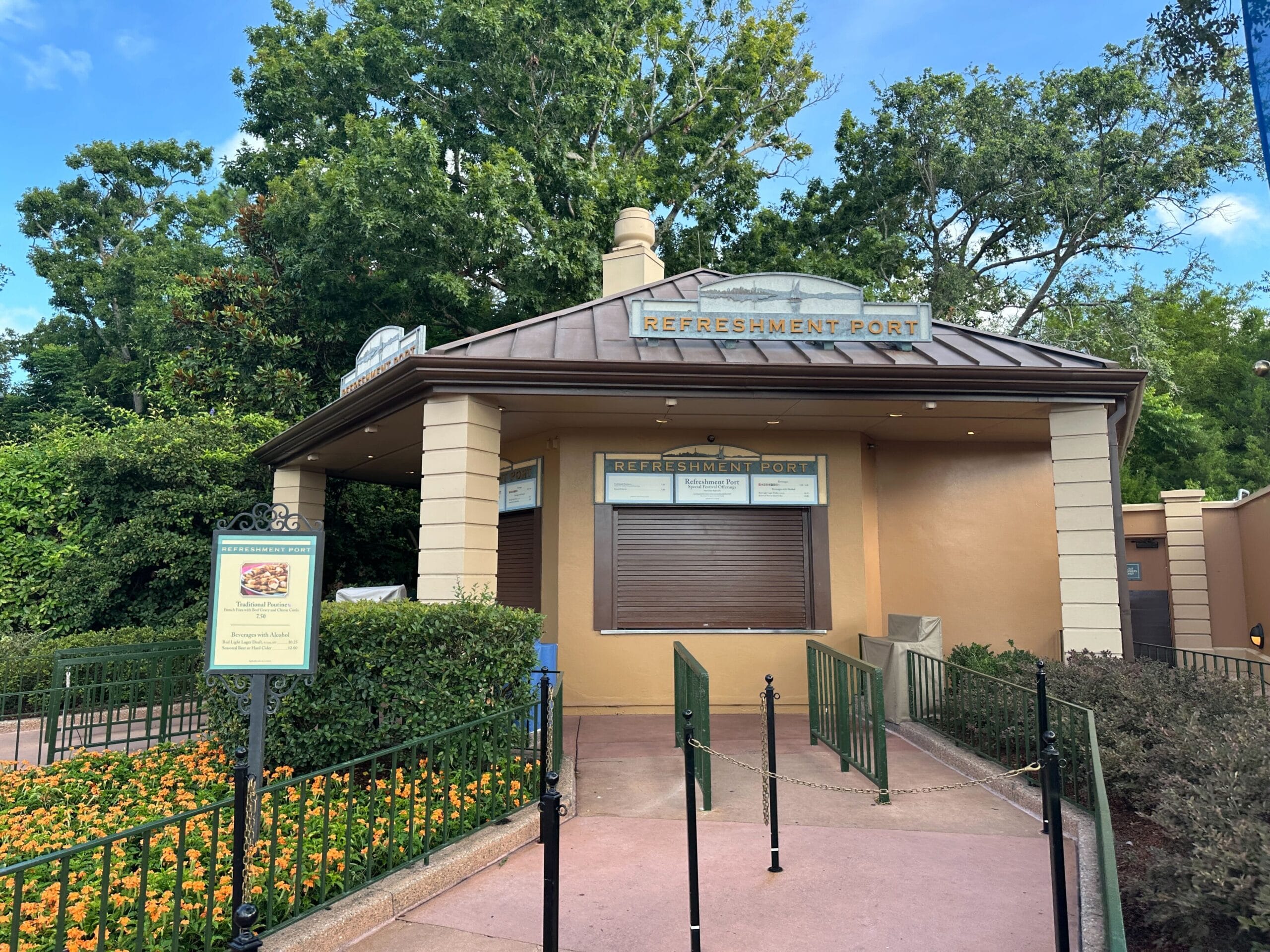 A closed refreshment stand with brown shutters, surrounded by greenery, prepares for the 2025 EPCOT International Food & Wine Festival.